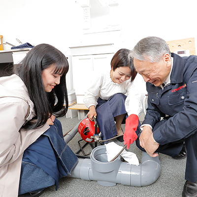 排水マスの補修について教える講師とそれを学ぶ学生